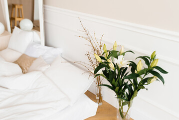White lily flowers in a vase, tree branches in a vase near the bed. Details of the interior decor of the house