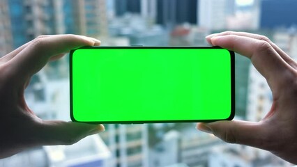 Close up male hands horizontal holding smartphone with green screen. Cityscape background. - Powered by Adobe