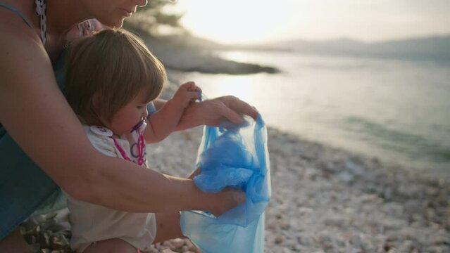A child with his mother collects garbage by the ocean. The family cleans the beach from plastic and waste, environmental protection.