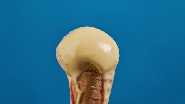 Timelapse of banana ice cream with cherry or strawberry topping in waffle cone melting on blue background. Delicious yellow ice cream melting. Close-up of sweet dessert. Food concept