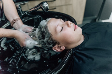 Fototapeta na wymiar Woman applying shampoo and massaging client's hair. A woman washing her hair at a hairdresser.