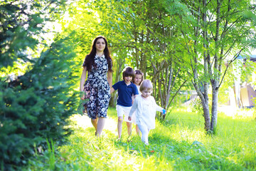 Fototapeta premium Young large family on a summer morning walk. Beautiful mother with children is playing in the park.