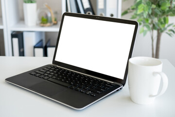 Fototapeta premium Computer mockup. Digital technology. Work place. Opened laptop with blank screen staying on desk with cup of coffee in light room interior.
