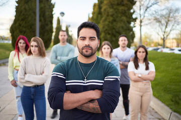 Latin man looking seriously at the camera while standing in front of a group of people. Concept of team and leadership.