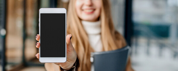 Happy smiling woman showing mobile phone against the background of the office center. Mockup for design