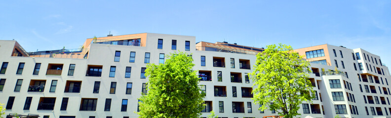 Fototapeta premium Ecological housing architecture. A modern residential building in the vicinity of trees. Ecology and green living in city, urban environment concept. Modern apartment building and green trees.