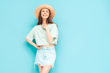 Portrait of young beautiful smiling female in trendy summer jeans skirt. carefree woman posing near blue wall in studio. Positive model having fun indoors. Cheerful and happy. In hat