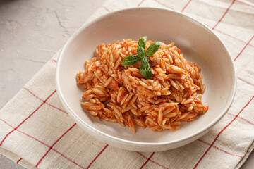 Homemade italian dish pasta risoni with tomato basil sauce in a deep bowl on checkered napkin