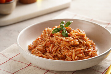 Homemade italian dish pasta risoni with tomato basil sauce in a deep bowl on checkered napkin