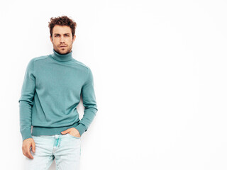 Portrait of handsome confident  model. Sexy stylish man dressed in blue sweater and jeans. Fashion hipster male with curly hairstyle posing near white wall in studio. Isolated