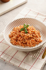 Homemade italian dish pasta risoni with tomato basil sauce in a deep bowl on checkered napkin