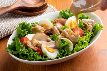 焼いた鶏肉と野菜のグリルチキンサラダに胡麻ドレッシングをかける