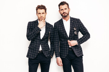 Portrait of two handsome confident stylish hipster lambersexual models. Sexy modern men dressed in black elegant suit. Fashion male posing in studio near white wall