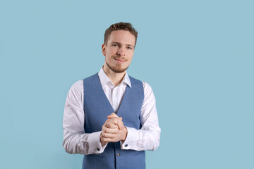 Portrait handsome man smiling against blue background with copy space. Smiling caucasian guy in white shirt and blue vest standing on blue background Successful caucasian man looking at camera