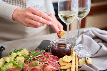 woman dips parmesan cheese into sauce, Two glasses of white wine and Italian antipasto meat platter