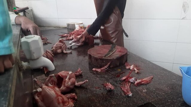 Men cutting raw chicken meat at the outdoor workshop in India. Butcher cutting pieces of chicken meat waiting for customers.