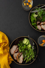 Hearty delicious lunch, fresh salad with cucumbers and microgreens of peas and with stewed pork, top view of the dark table with food