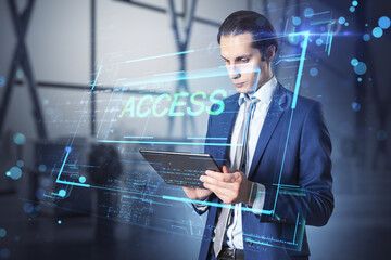Attractive young european businessman using tablet in blurry office interior with access hologram. Technology and data concept. Double exposure.