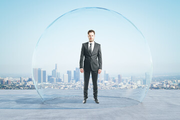 Attractive young european businessman standing under and inside big glass sphere cover on concrete...