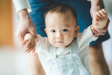 toddler baby learning to walk and having support by family together, little child with father and mother at home with first step to walking by help and holding hand from dad, happy childhood help care