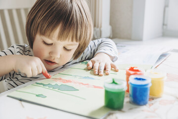 Finger painting. Portrait of cute little boy painting with fingers at home. Close-up of child's hand in colorful paints. Early education concept. Sensory play. Development of fine motor skills.