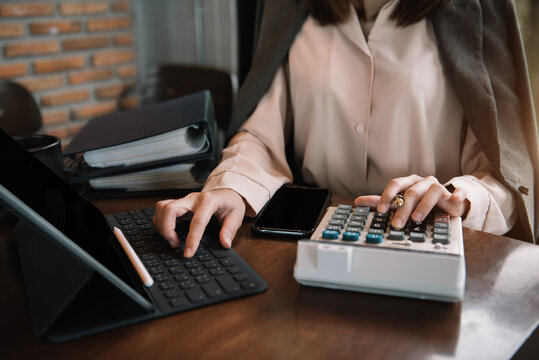 Business woman working on desk office with using a calculator and tablet to calculate the numbers.