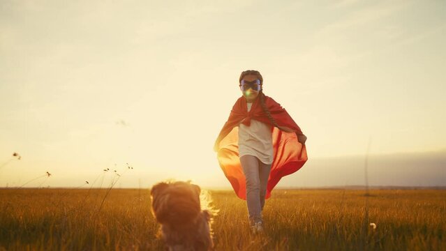girl superhero. child in a red raincoat runs with a dog outdoors in the park. happy family kid dream concept. little girl superhero lifestyle runs with a dog across the field in nature