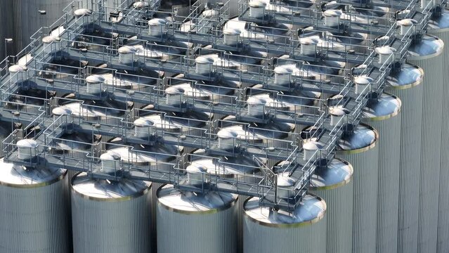 Catwalk over industrial holding tanks and beer brewery. Distillation and fermentation process stainless steel silo. Aerial.