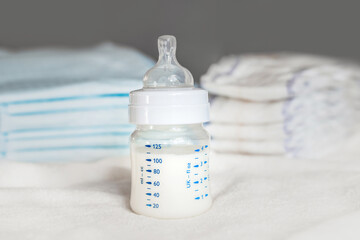 Baby bottle with milk and diapers on a white fabric background. Baby care. First days of life. Feeding and motherhood