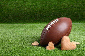 American football ball and hearts on green grass. Space for text