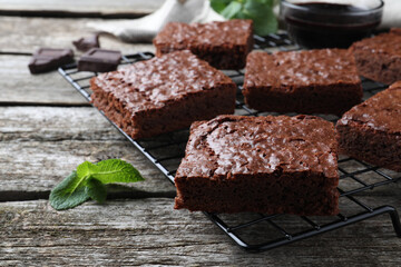 Cooling rack with delicious chocolate brownies and fresh mint on wooden table, closeup