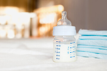 Baby bottle with milk and diapers on a white fabric background. Baby care. First days of life. Feeding and motherhood