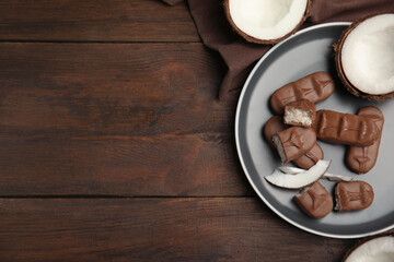 Delicious milk chocolate candy bars with coconut filling on wooden table, flat lay. Space for text