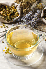 Glass cup of aromatic freshly brewed tea near different dry herbs on wooden table