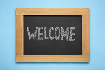 Obraz premium Small chalkboard with word Welcome on light blue background, top view