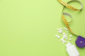 Jar of weight loss pills and measuring tape on green background, flat lay. Space for text