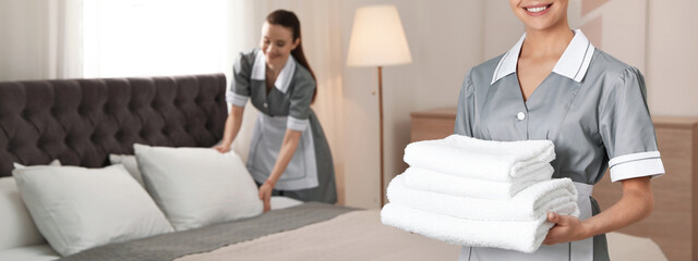 Chambermaid with stack of fresh towels in hotel room, closeup view with space for text. Banner...