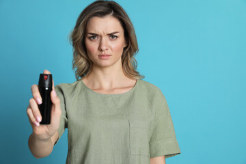 Young woman using pepper spray on turquoise background