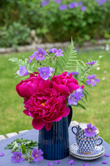 Blumenstrauß mit pink Pfingstrosen, Glockenblumen und Storchschnabel in Vase im Garten