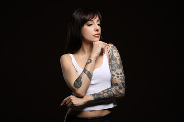 Obraz na płótnie Canvas Beautiful woman with tattoos on arms against black background