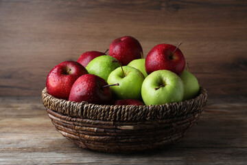 Fresh ripe green and red apples with water drops in wicker bowl on wooden table