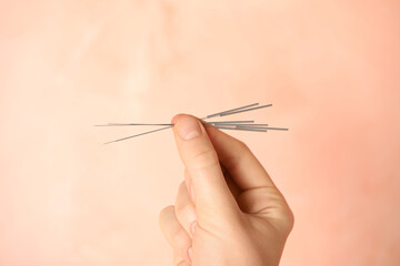 Woman holding needles for acupuncture on pink background, closeup