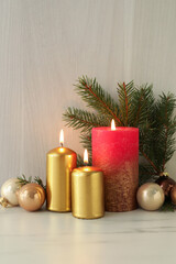 Burning candles with Christmas baubles and fir tree branch on table against wooden background