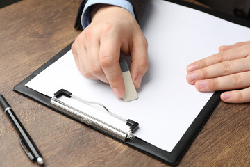 Man erasing something on paper at wooden table, closeup