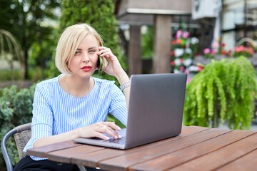 Portrait business woman talking on smartphone use notebook laptop at coffee cafe outdoors. Beautiful girl at desk computer online business call.