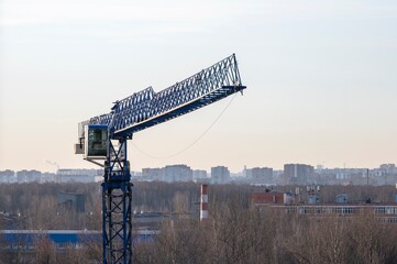 A construction crane while working at a construction site in the rays of the evening sun against the background of the skyline and city buildings.