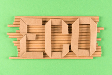 Kraft paper drinking straws and paper letters word ECO over green background. Sustainable lifestyle and zero waste concept. Ethical consumerism. Flat lay