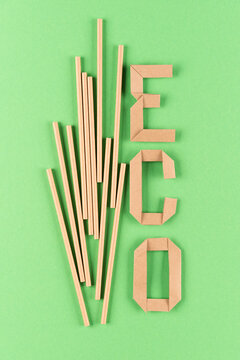 Vertical image of eco kraft paper drinking straws and paper letters word ECO over green background. Sustainable lifestyle and zero waste concept. Ethical consumerism. Flat lay