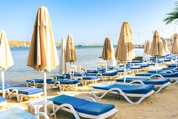 Empty beach loungers without people in quarantine of pandemic, start or the end of summer vacation season . Umbrella on a sunbed near the sea and ocean on vacation with travel and tourism. Hotel, tour