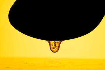 Fototapeta na wymiar Honey dripping, pouring from dark spoon on yellow background. Thick viscous honey molasses flowing. Close up of golden honey liquid, sweet product of beekeeping. Sugar syrup is pouring.